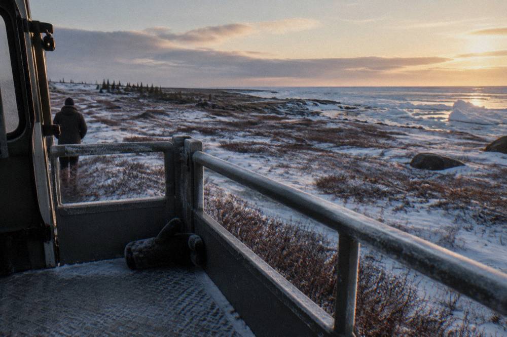 The open rear viewing deck of a tall tundra vehicle overlooking flat subarctic tundra and a frozen bay