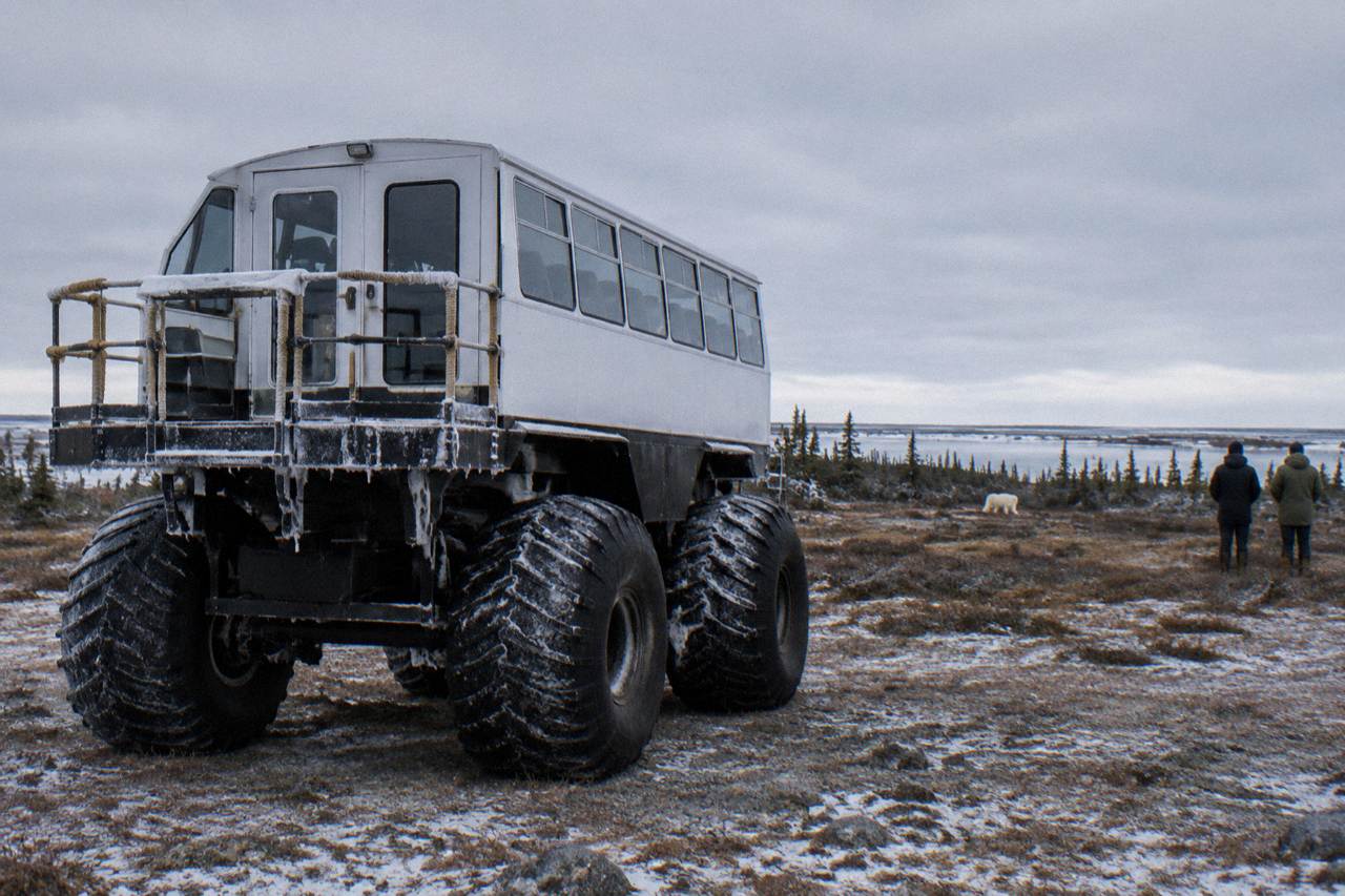 A large raised tundra vehicle with oversized tires parked on open subarctic terrain near Churchill