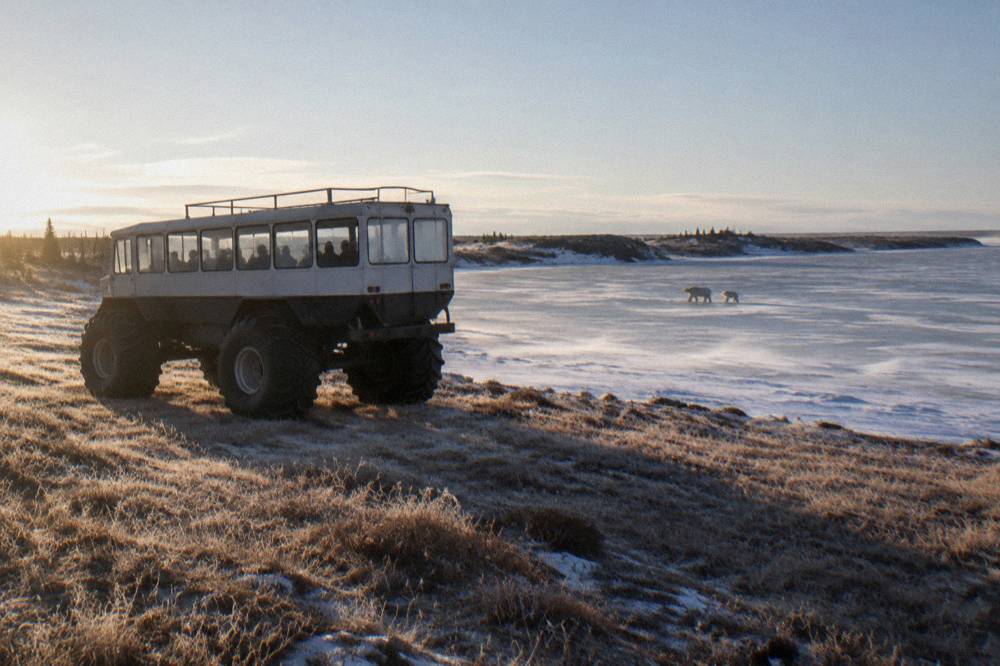 A large raised tundra vehicle with tall tires parked on open tundra near a frozen pond