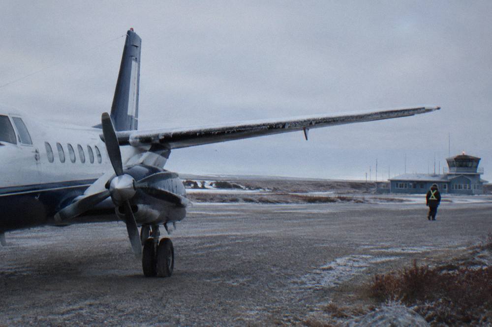 A small aircraft on a gravel-edged runway beside flat tundra and low cloud