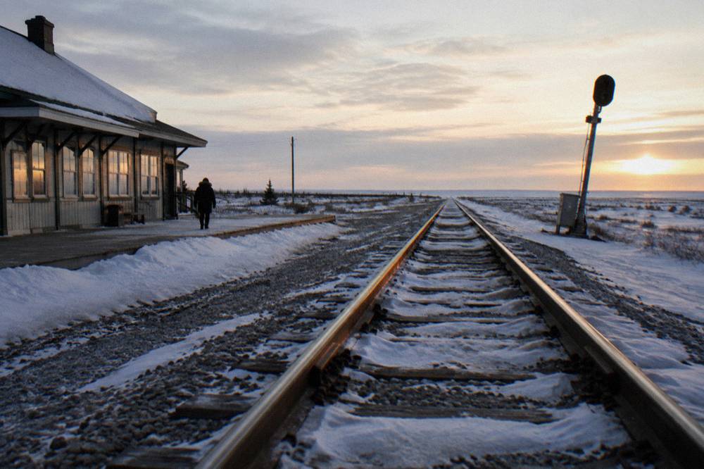 Railway tracks stretching straight across flat tundra toward a distant horizon