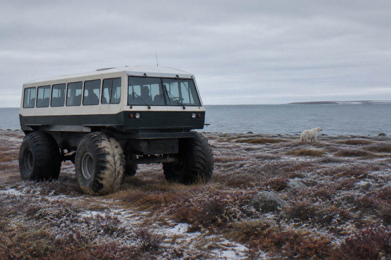 A raised tundra vehicle parked on open coastal tundra near Hudson Bay under a wide grey sky
