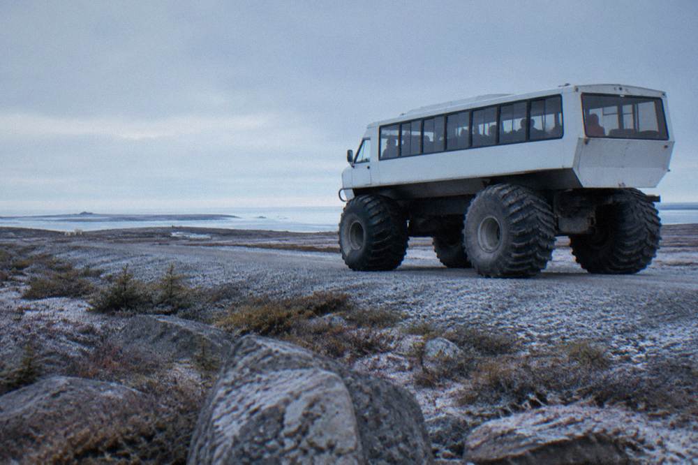 A large raised tundra vehicle on a gravel trail across open tundra