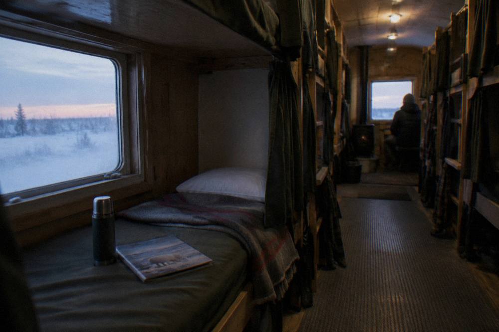 Rows of bunks with curtains and small windows inside a mobile tundra lodge vehicle