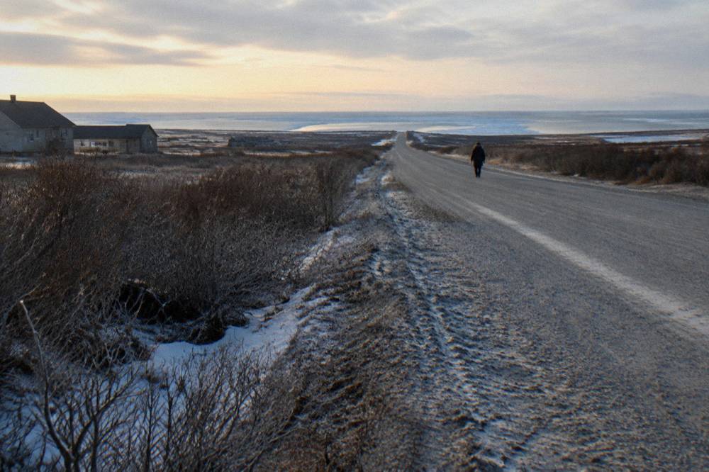 A wide gravel road leading out of Churchill across flat tundra toward the coast