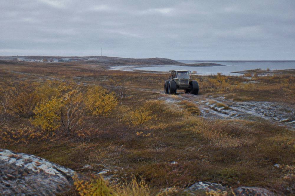 A purpose-built Tundra Buggy vehicle with large tires crossing open tundra near Churchill in autumn.