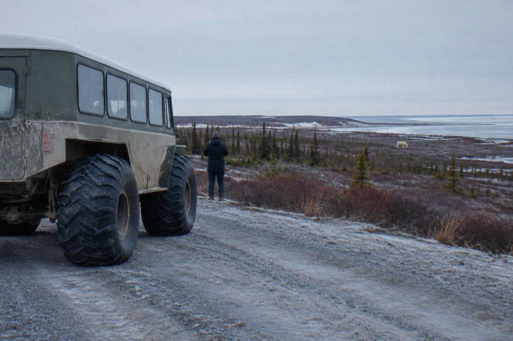 A large wheeled tundra vehicle parked on a gravel road beside frozen tundra