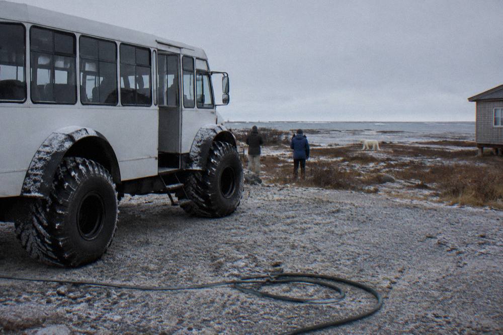 A large-wheeled tundra vehicle parked on a gravel road under a grey Arctic sky