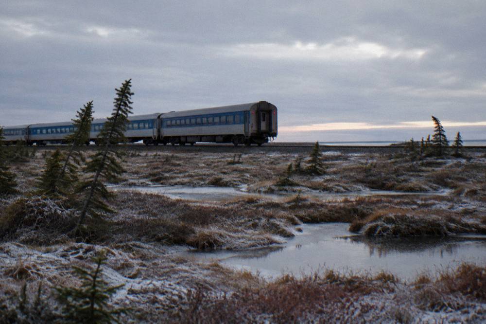 A passenger train crossing vast open subarctic muskeg under a wide grey sky