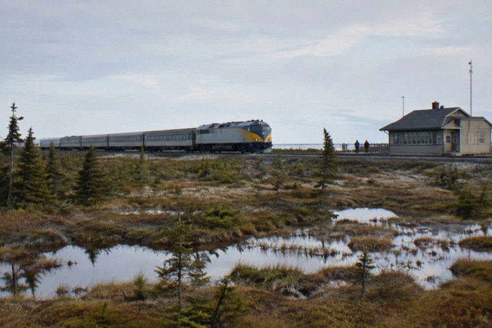 A passenger train crossing vast wet muskeg flats under a wide northern sky.
