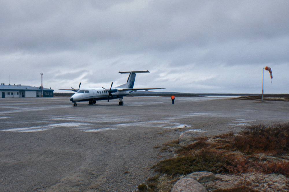 A small aircraft on a gravel-and-asphalt northern airstrip under low clouds.