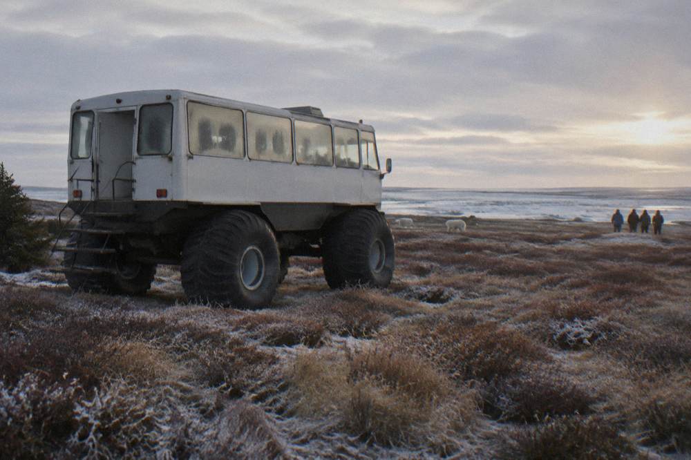 A purpose-built raised tundra vehicle parked on open subarctic terrain near the coast.