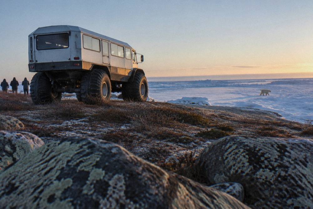 A large all-terrain tundra vehicle with huge tires parked on open ground near a frozen bay