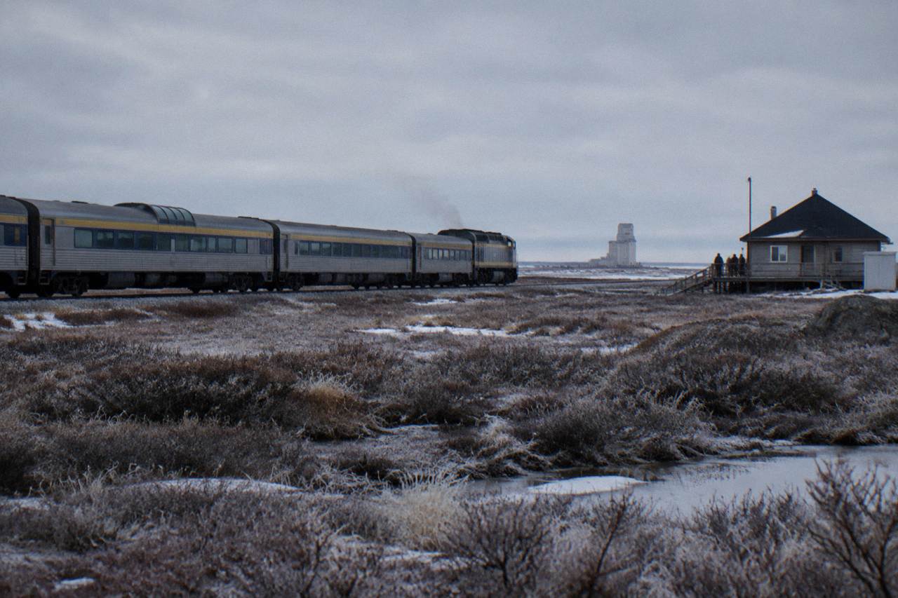 A passenger train crossing wide open subarctic tundra under a low grey sky