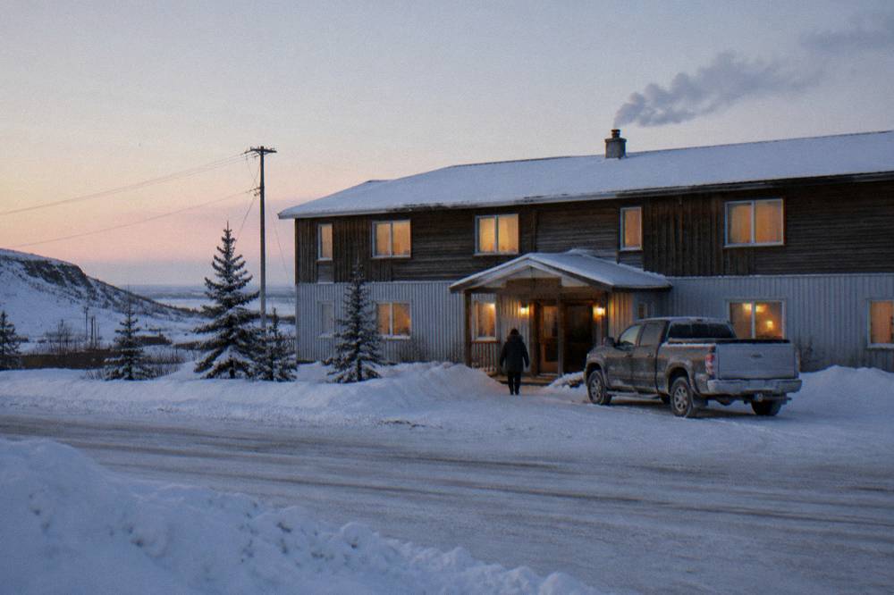 A hotel exterior at dawn with a tour vehicle parked outside under a pale northern sky