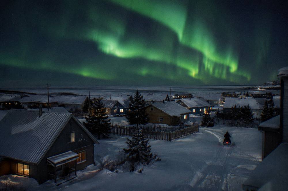Green aurora curtains over a snow-covered Churchill landscape at night