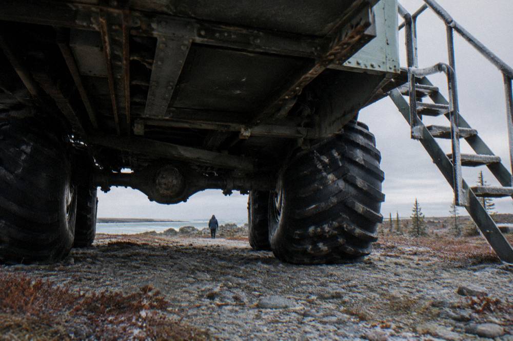 A large raised tundra vehicle with huge tires parked on open subarctic ground