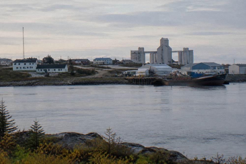 A small northern town of low buildings beside a wide river estuary under a pale sky