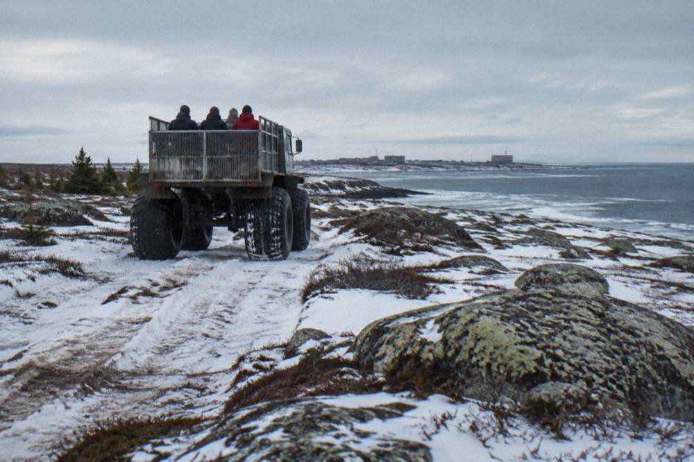 A large raised tundra vehicle on open snowy terrain near the coast in daylight