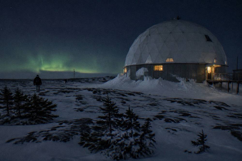 A domed structure on a dark snowy plateau with a faint green aurora glow on the horizon