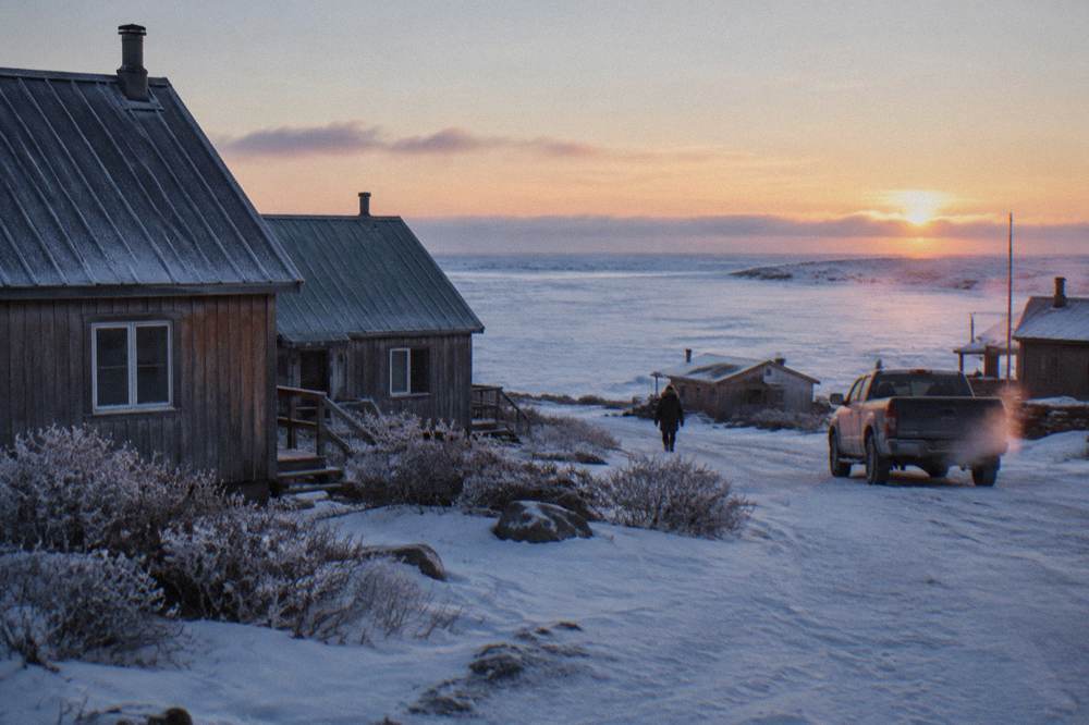 A small northern town of low buildings beside a wide frozen bay at first light