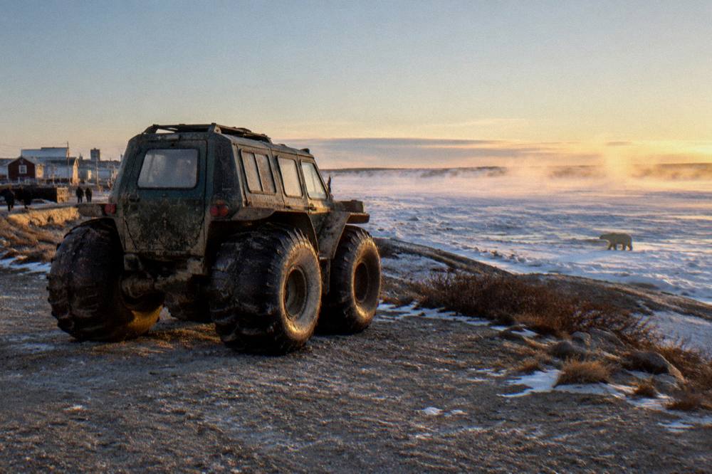 A tall-wheeled tundra vehicle standing on open ground near a frozen bay shoreline