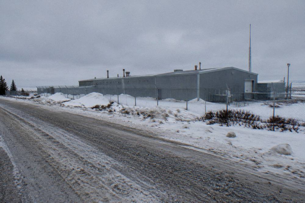 A signpost with bear warning signage standing beside a coastal gravel road