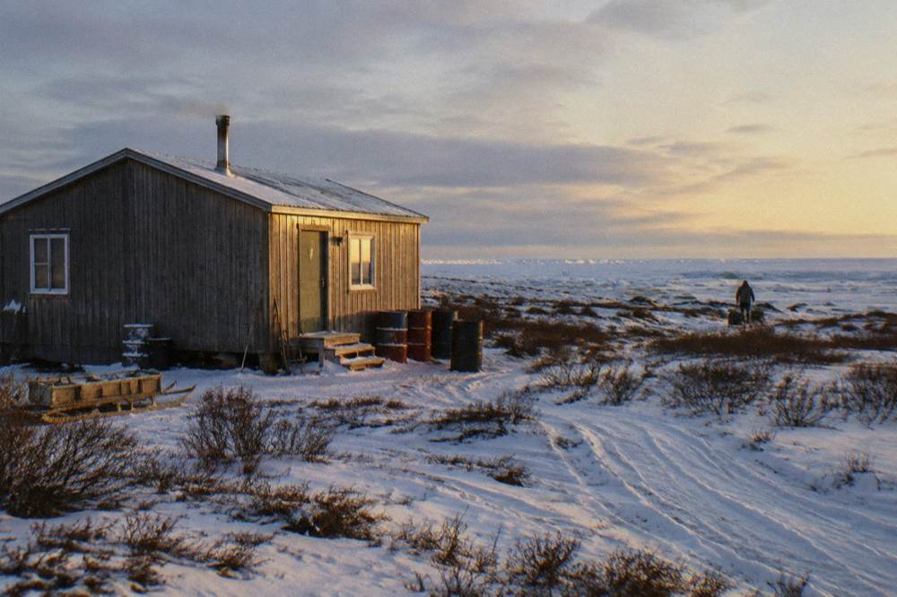 A small lodge building on a remote stretch of snow-dusted coastline with sea ice visible on the horizon