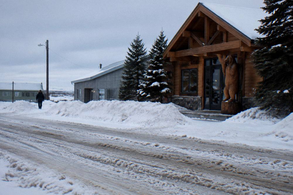 A quiet northern town street with low buildings, snow banks and a lodge-style wooden facade under a pale sky
