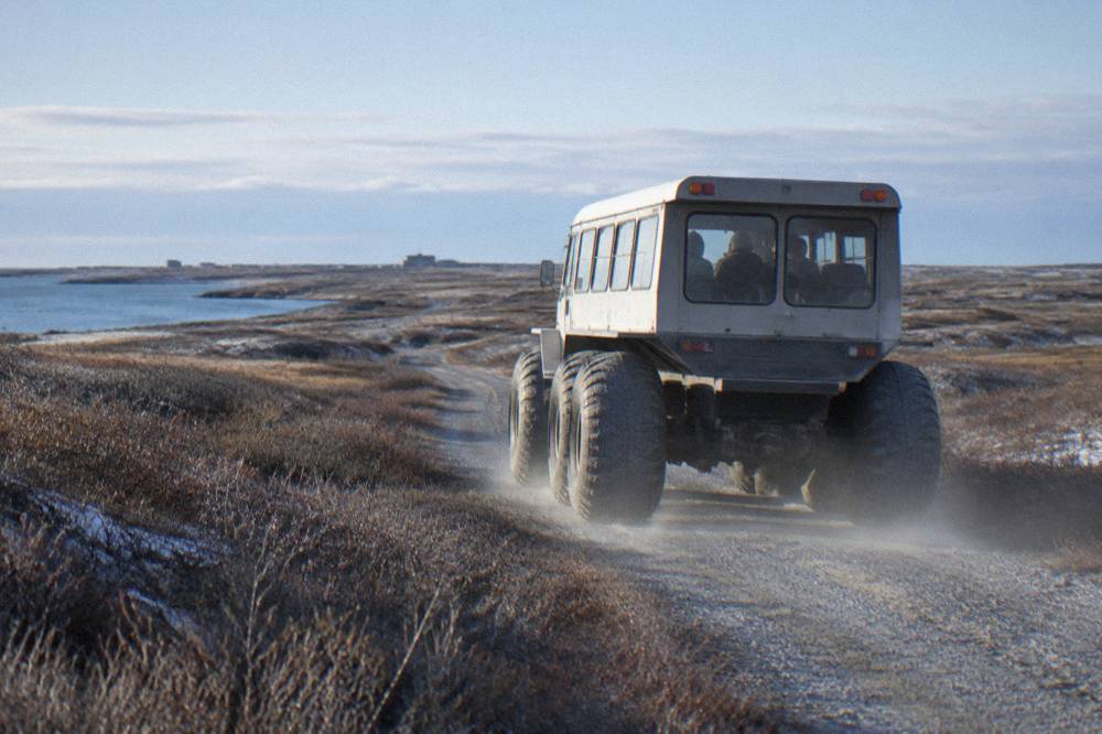 A raised tundra vehicle on a gravel trail through flat coastal tundra