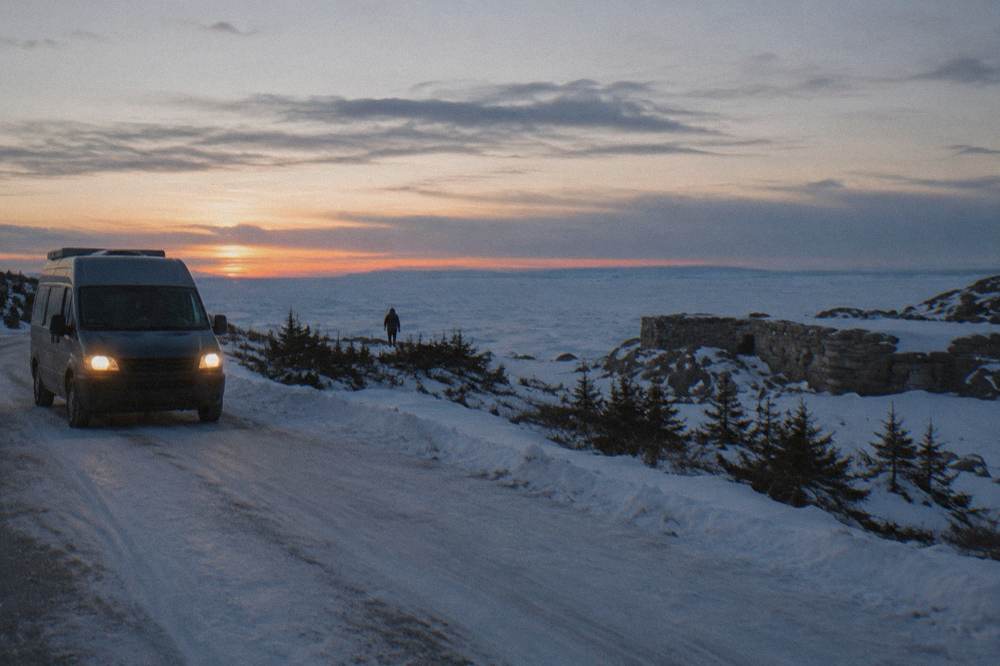 A snowy coastal road at dusk with a parked vehicle and open horizon toward frozen Hudson Bay
