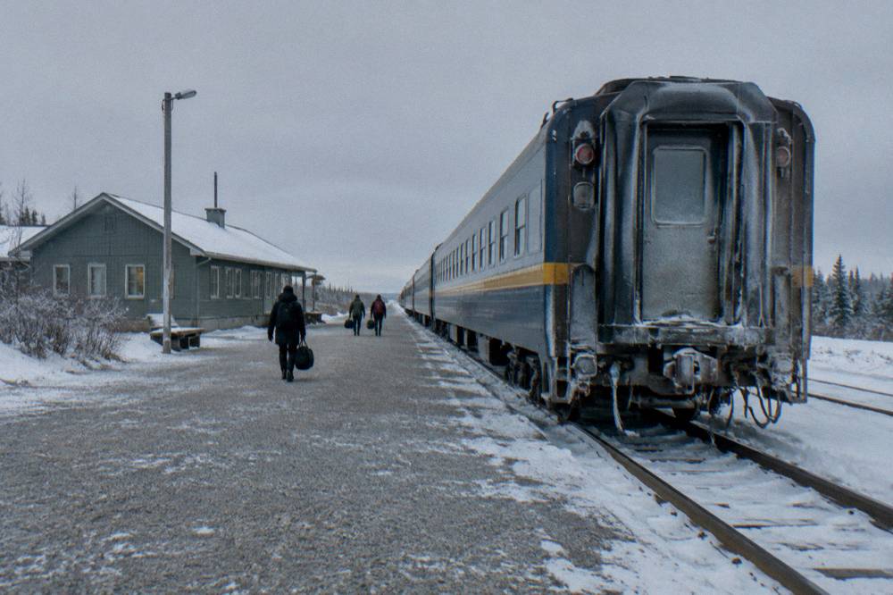A passenger train on a rail line crossing open snowy subarctic landscape toward a northern town