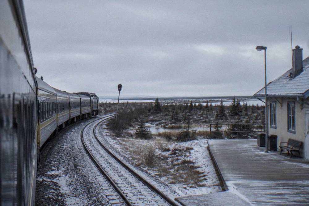 A passenger train on rails crossing flat northern forest and wetland