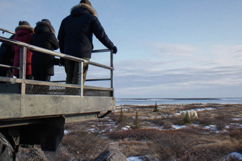 Travellers watching from the open rear deck of a large raised tundra vehicle