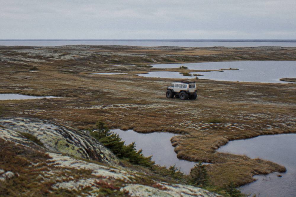 A raised tundra vehicle with large tires crossing flat open tundra dotted with ponds