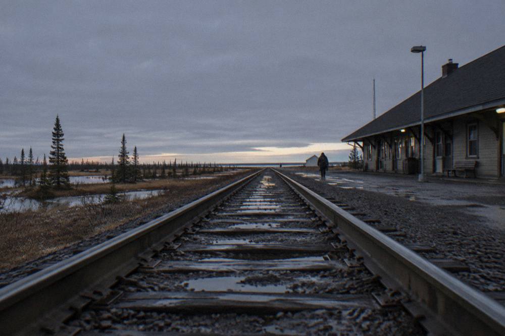 A rail line crossing flat muskeg and scattered black spruce trees toward the horizon
