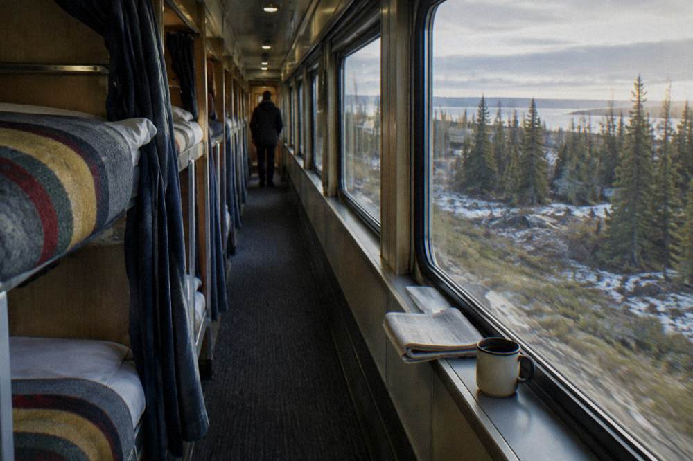 A sleeper car corridor with made berths beside large windows showing forest