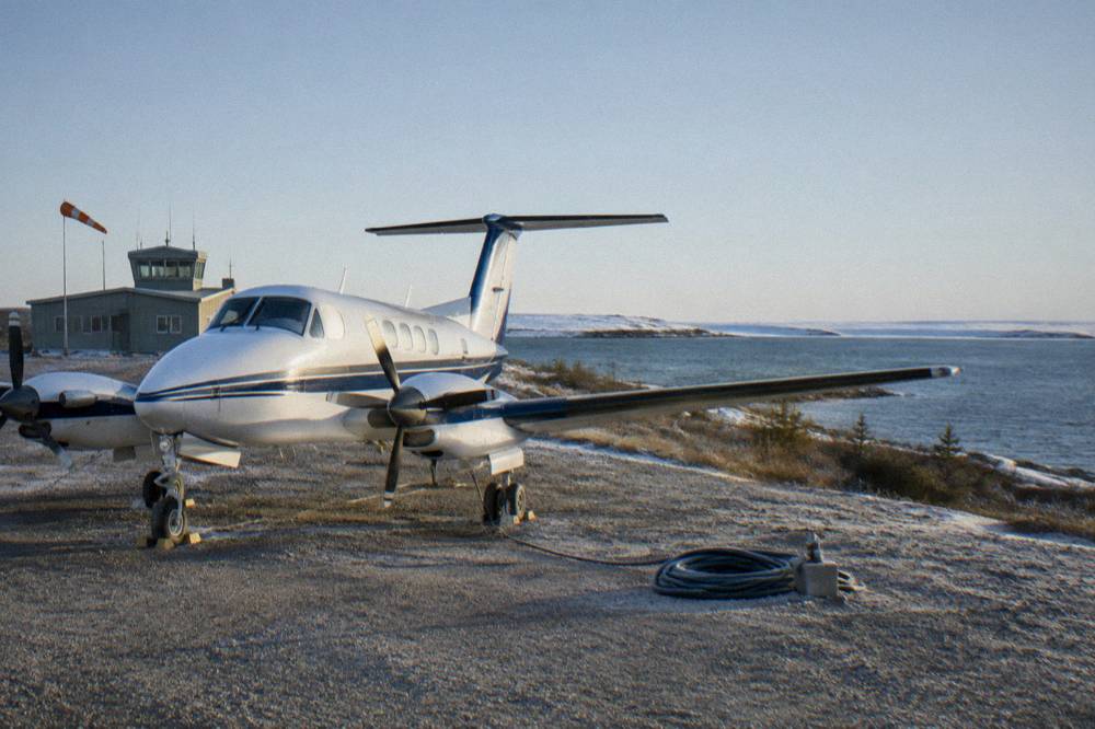 A small turboprop aircraft parked on a northern runway beside cold grey water